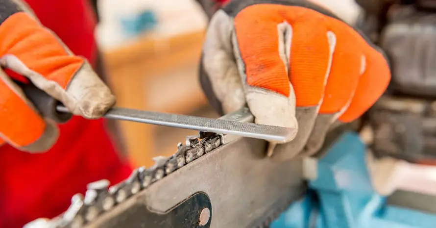 A man in gloves sharpens a chainsaw
