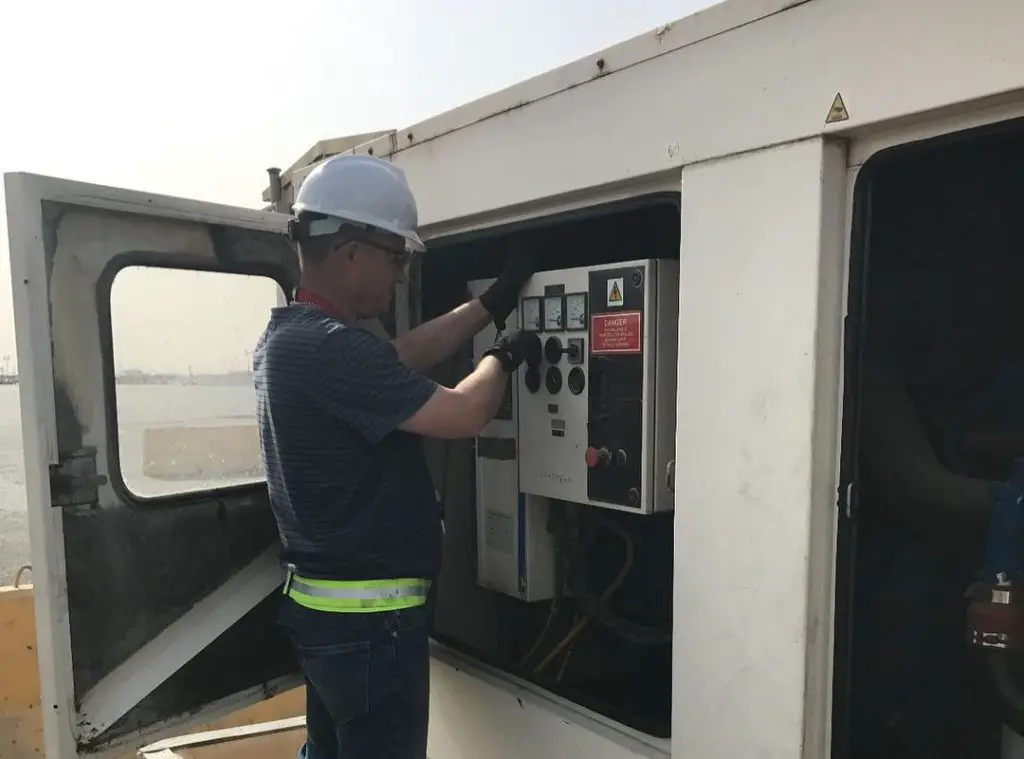 A specialist in a helmet maintains a white generator 