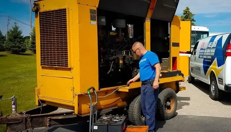 A worker in a blue T-shirt maintains a large yellow generator