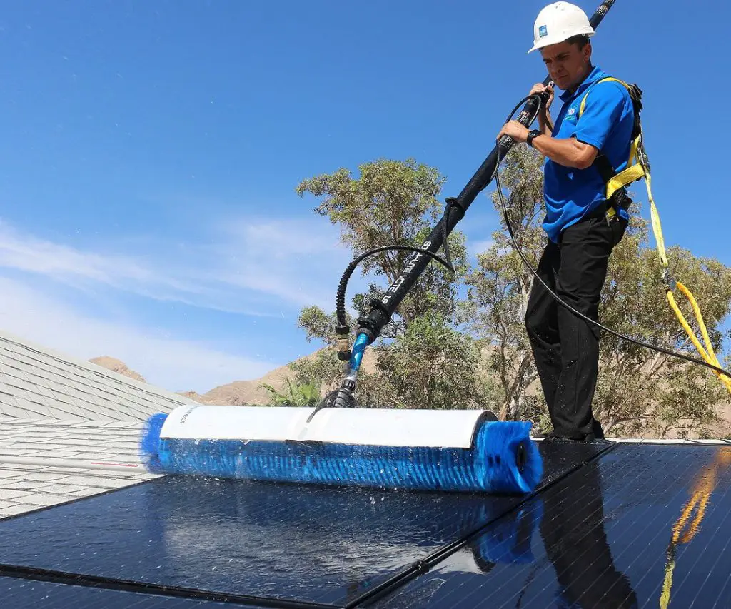 A worker maintains solar panels on the roof